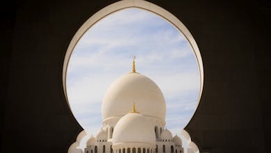 Captivating view of white domes of Sheikh Zayed Grand Mosque through an archway against the blue sky.