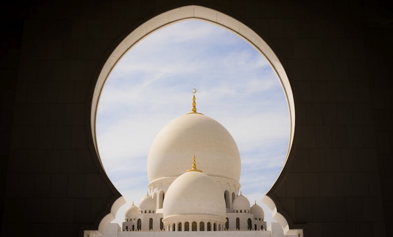 Captivating view of white domes of Sheikh Zayed Grand Mosque through an archway against the blue sky.