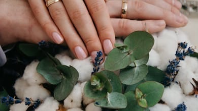 Close-up of couple's hands with gold wedding bands over a floral bouquet.